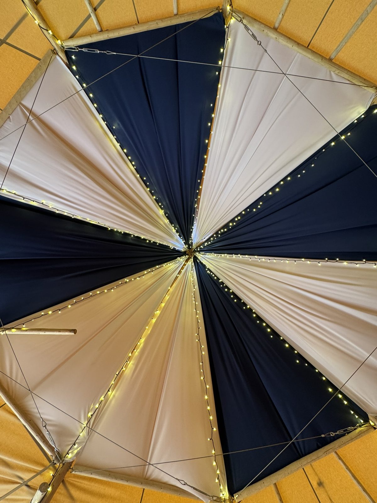 Looking straight up at the crown of the Cransley tipi: dark blue and white panels radiating with fairy-lit seams