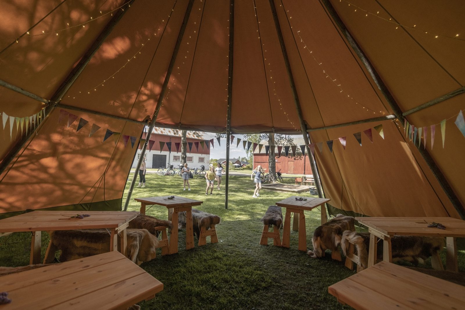 Interior view of outdoor tipi looking out through entrance with benches and bunting