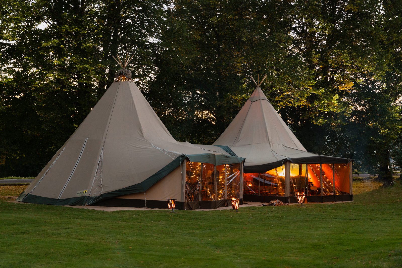Two outdoor tipi classrooms glowing warmly at dusk in natural setting, ideal for state school outdoor learning provision