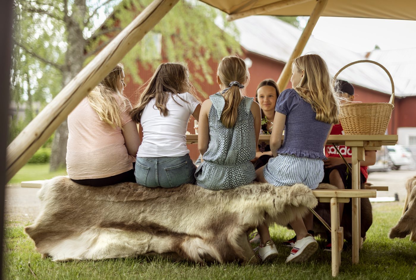Children sitting together on a bench in outdoor tipi classroom, engaged in learning and collaboration in independent schools
