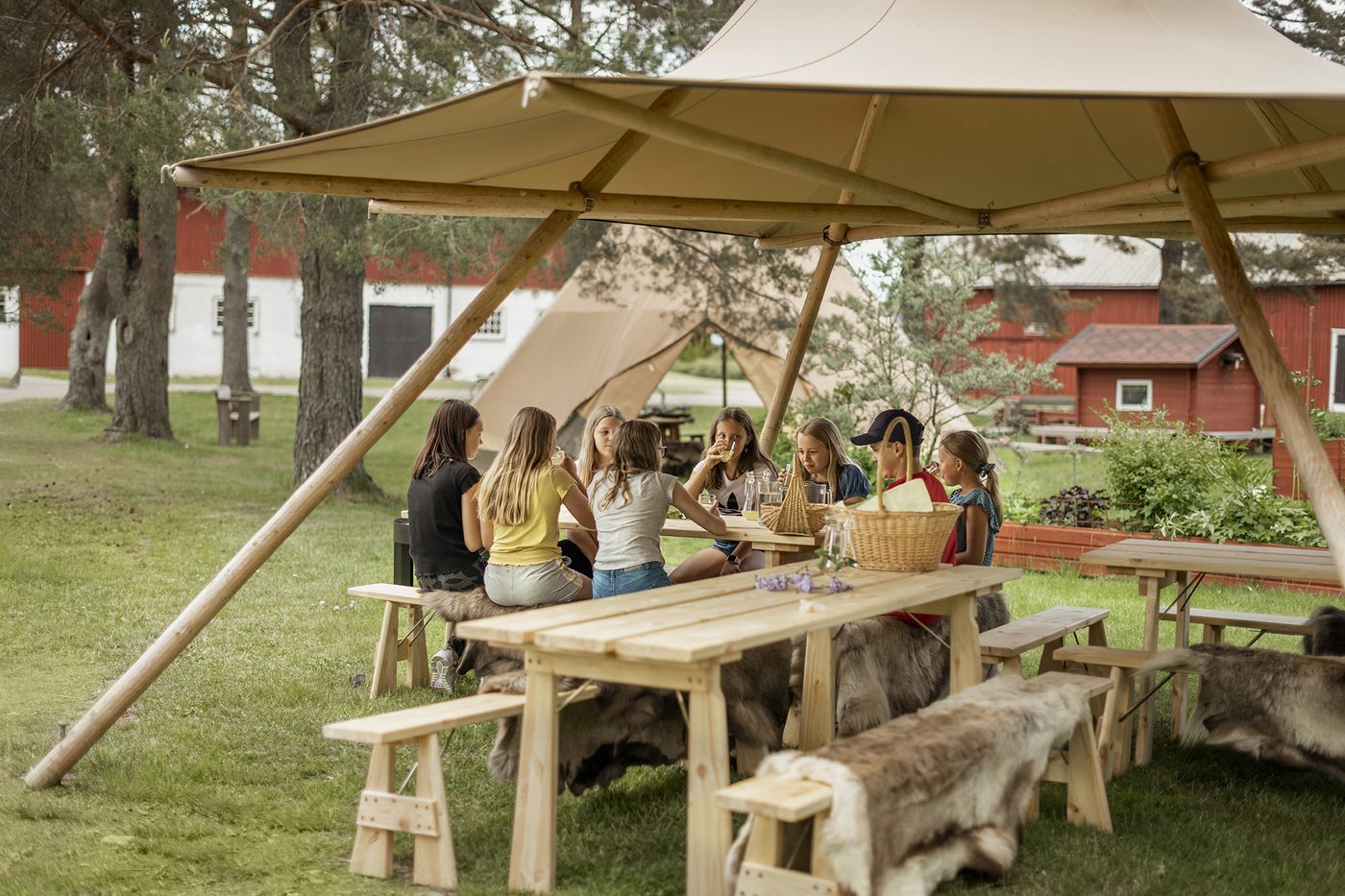 Group of children gathering and learning together under The Bower forest school shelter in natural outdoor setting