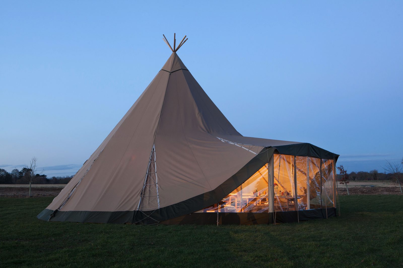A Beehive Stratus 72 tipi at dusk with WallFlex extension glowing warmly — outdoor classroom for Welsh schools