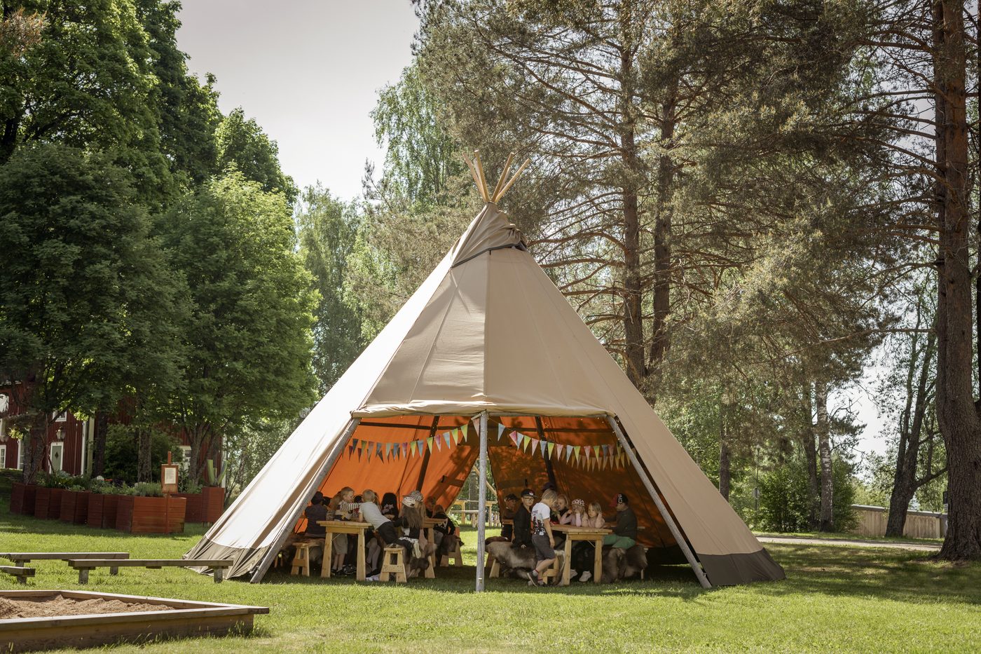 Children gathering outside beautifully decorated tipi outdoor classroom in woodland setting with bunting