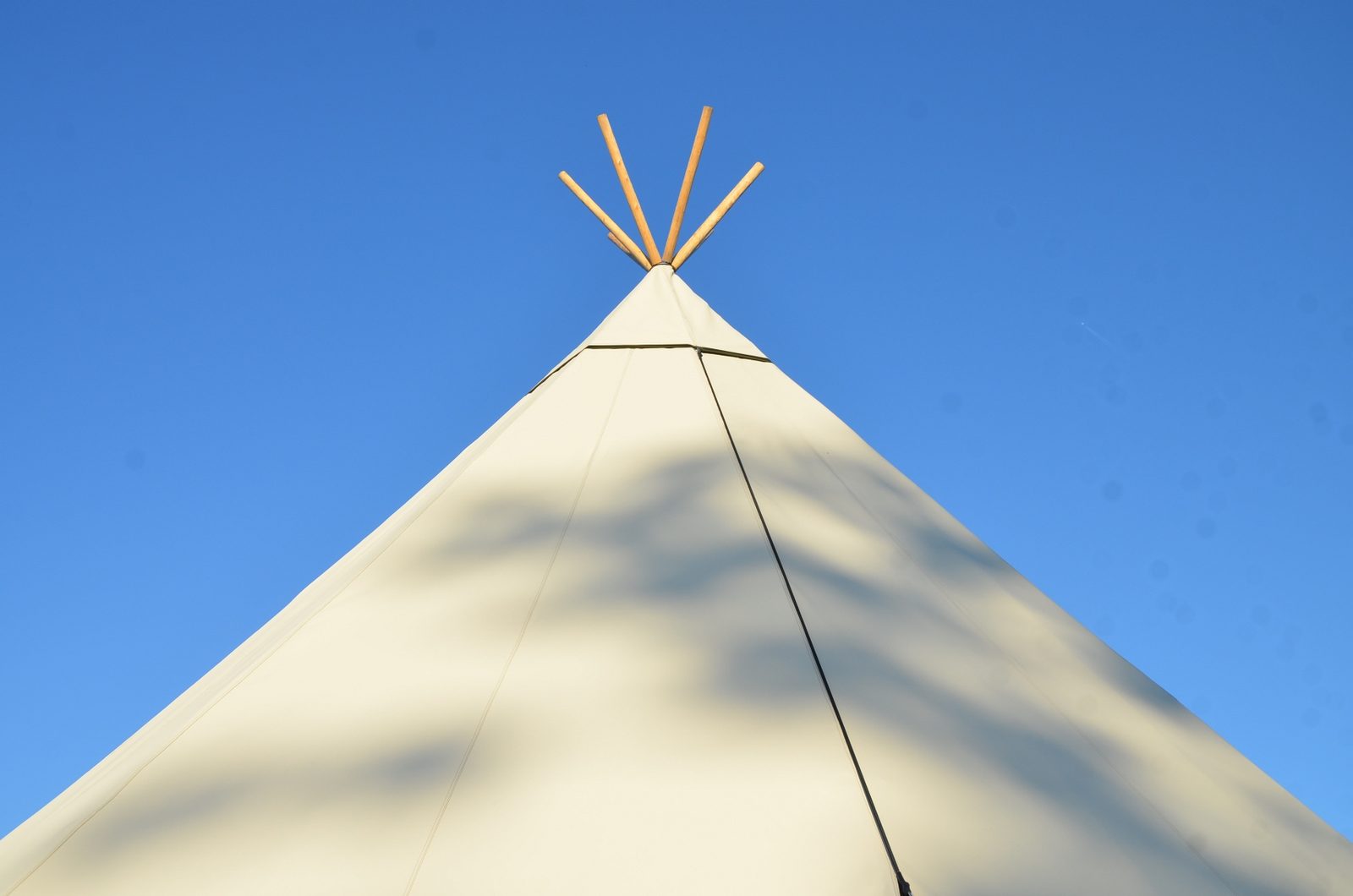 A white canvas tipi peak with dappled shade in bright summer sun against a blue sky